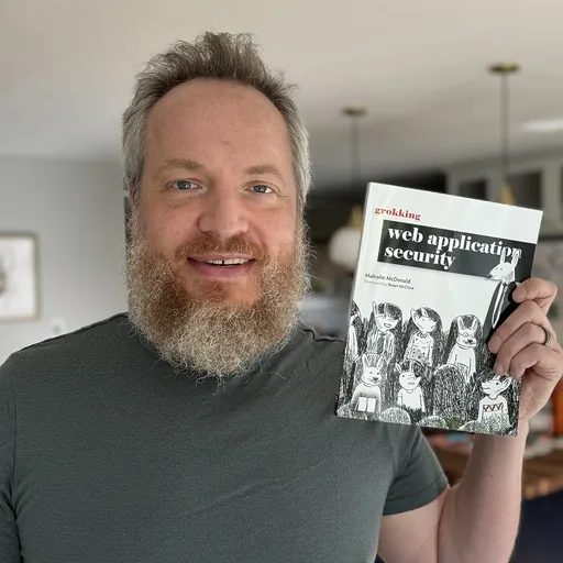 Malcolm McDonald, Founder and Editor-in-Chief of Hacksplaining, holding a copy of his book Grokking Web Application Security
